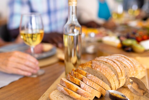 close-up of bread slices on wooden board with white wine bottle on dining table in nursing home. baked, food, alcohol, fresh, unaltered and meal concept.