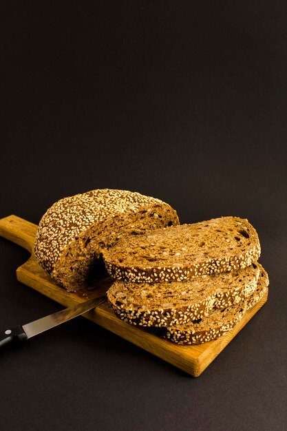 Close-up on bread with sesame on the wooden cutting board on the black background. Location vertical.