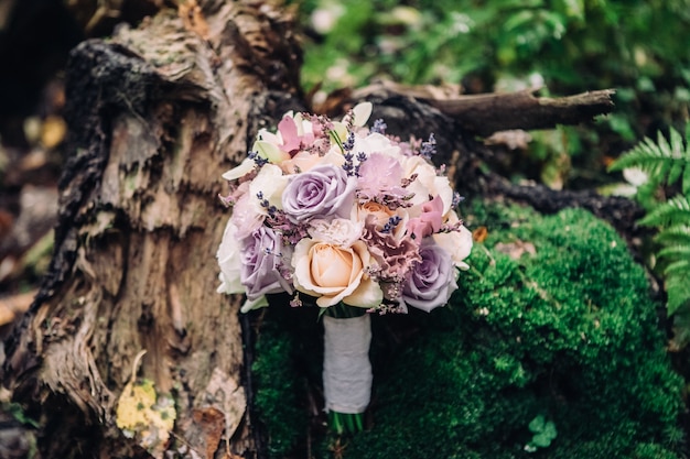 Close-up bridal bouquet of roses in lilac pink on a blurred background of forest and moss, selective focus