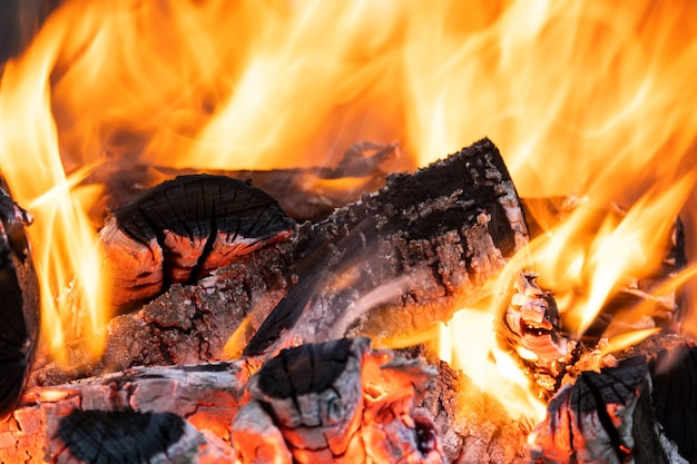 Close up of brightly burning wooden logs with yellow hot flames of fire at night.