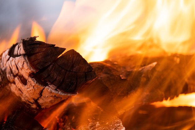 Закройте ярко горящих деревянных бревен с желтым горячим пламенем огня ночью.