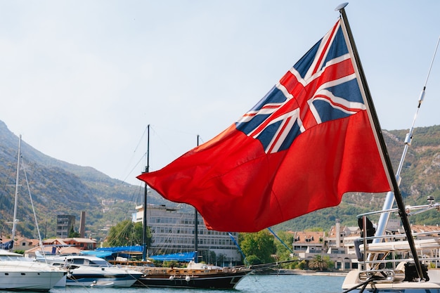 Close-up of the British Red Ensign aboard a ship with ships and mountains