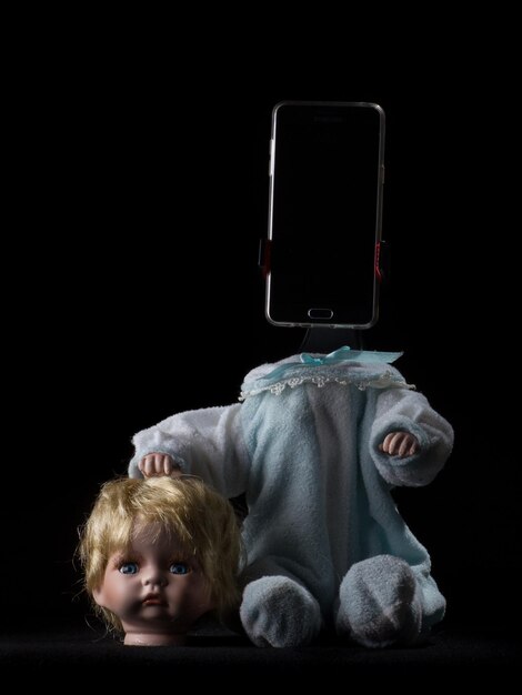 Photo close-up of broken doll with mobile phone against black background