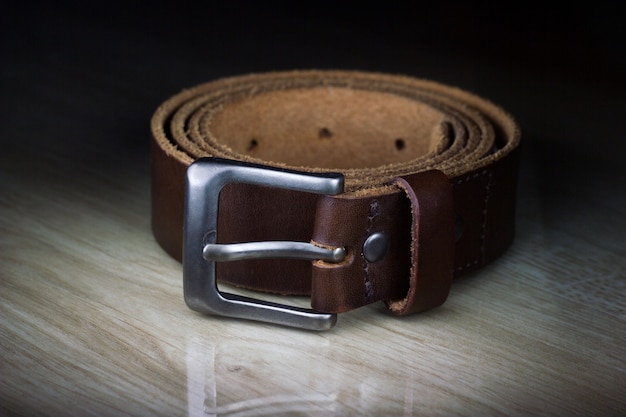 Close-up of brown leather belt on wooden table at night.