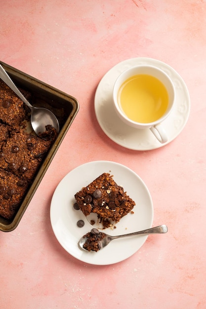 Close up brownies with chocolate chips and rolled oats served with cup of tea on pink background