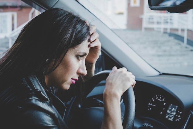 Photo close up of brunette girl looking frustrated sitting in car and leaning wheel car accident with female driver young woman feels sick or tired being at wheel profile view of worried lady in auto
