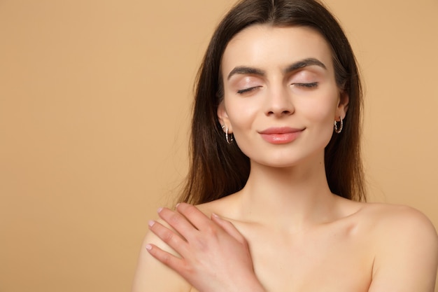 Close-up brunette half naakte vrouw 20s met perfecte huid hand op schouder geïsoleerd op beige pastel muur portret. huidverzorging gezondheidszorg cosmetische procedures concept.