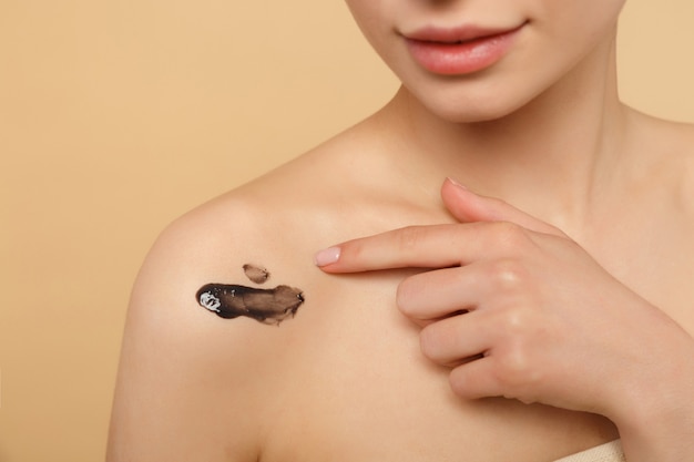 Photo close up brunette half naked woman with perfect skin, nude make up black mask isolated on beige pastel wall