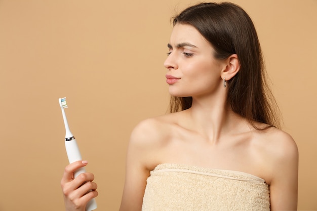 Close up brunette half naked woman with perfect skin, nude make up hold brush isolated on beige pastel wall