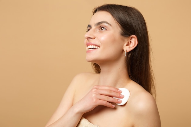 Close up brunette half naked woman with perfect skin, nude make up isolated on beige pastel wall