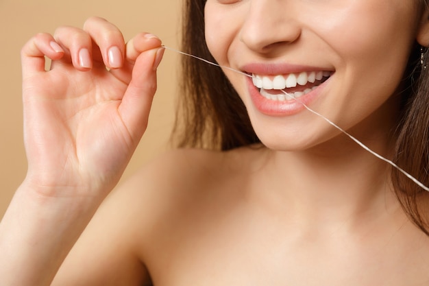 Close up brunette half naked woman with perfect skin nude make up using floss isolated on beige pastel wall