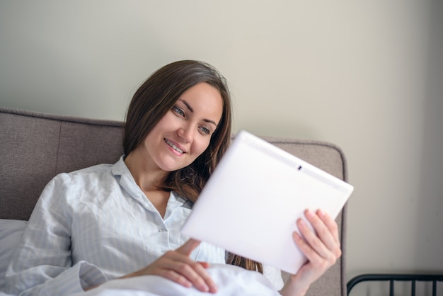 Close-up of brunette woman uses tablet lying in bed early in the morning