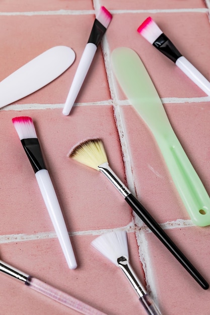 Close up of brushes and spatulas for applying face mask on pink tiled background