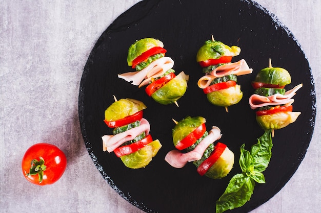 Close up of Brussels sprouts tomatoes cucumber and bacon sliders on slate board top view