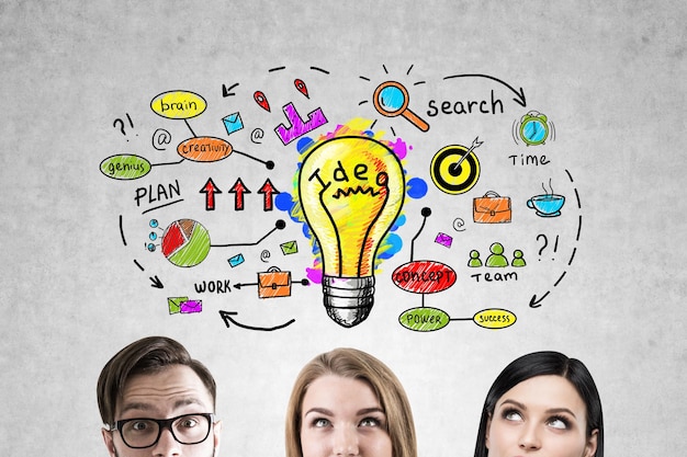 close up of a bsiness team members heads near a concrete wall with a bright idea sketch drawn on it.