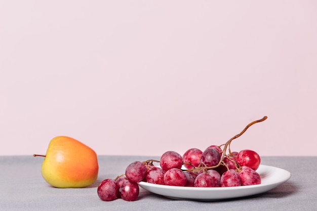 Close-up of a bunch of grapes and an apple on a pink background