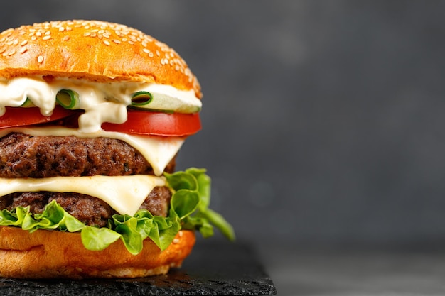 Close up burger with beef cutlets cheese cucumber lettuce on\
black background fast food