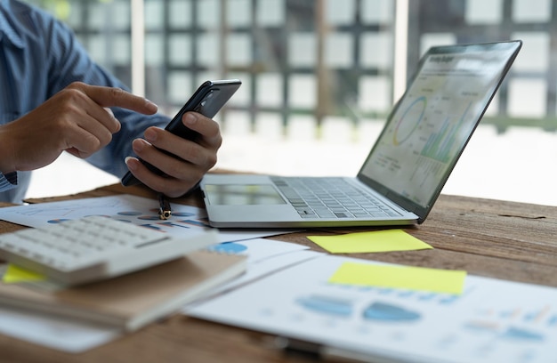 Close up business or accountant using mobile phone for\
analyzing chart and graph showing changes on the market and holding\
smartphone at office