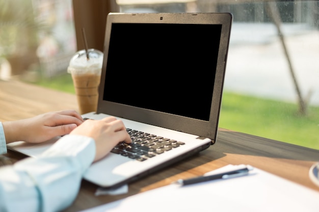 Il primo piano della femmina di affari che lavora con il computer portatile fa un documento e uno smartphone della nota in cof