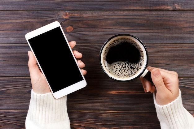 Close up business man's hand holds smart phone with black isolated screen over wooden background and coffee