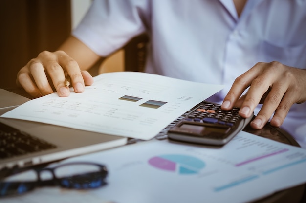 Close up Business man using calculator and laptop computer for calculating with finance paper, tax, accounting, Accountant concept.