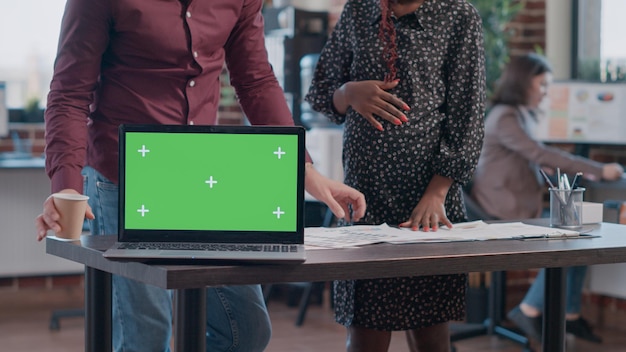 Primo piano di uomini d'affari che hanno laptop con schermo verde orizzontale sulla scrivania. donna incinta e collega che utilizzano modello di mockup isolato e sfondo con chiave di crominanza sul display.