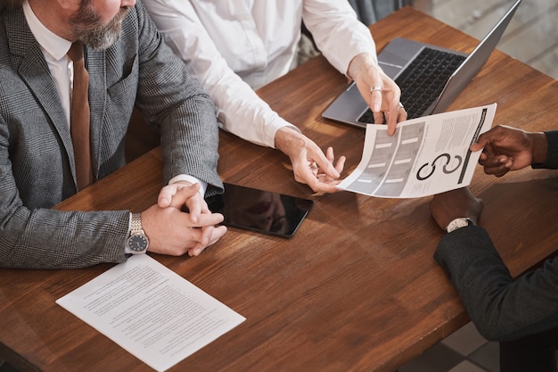 Close-up of business people sitting at the table at meeting businessman suggesting to read financial report to his partners