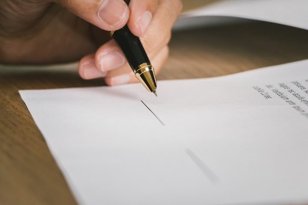 Close up business woman signing terms of agreement document on wooden table