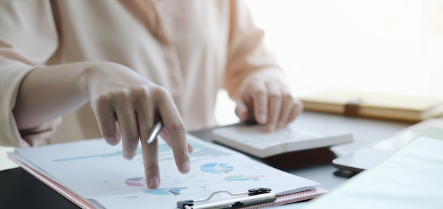 Close up business woman using calculator and checking a graph on a wooden desk in the office