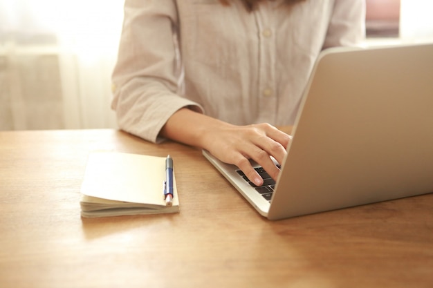 Chiuda sulla donna di affari che per mezzo del computer portatile sullo scrittorio di legno