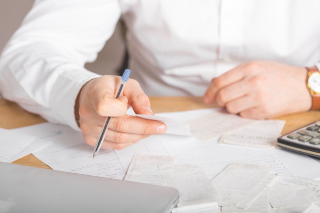 Close up of businessman or accountant hand holding pen working on calculator accountancy document and laptop computer at office, business concept