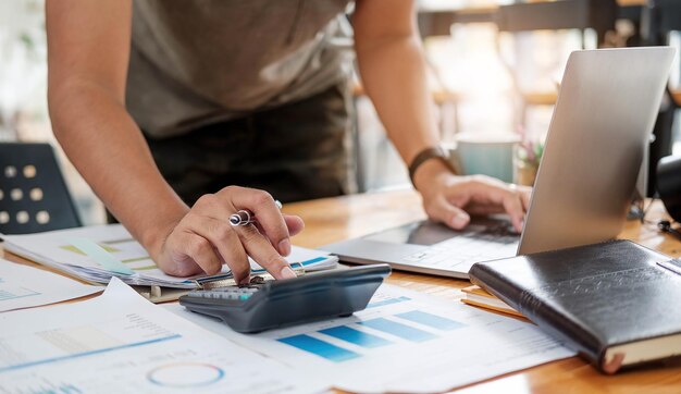 Close up of businessman or accountant hand holding pen working on calculator to calculate business data accountancy document and laptop computer at office business concept