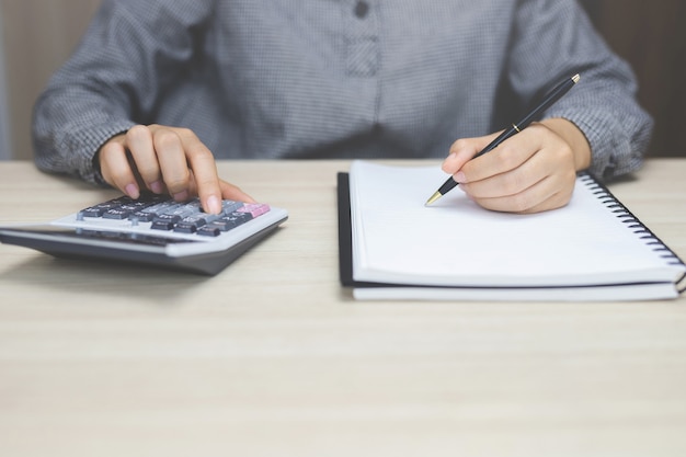 Close up of businessman or accountant hand holding pen working on calculator to calculate business data, accountancy document and laptop computer at office, business concept