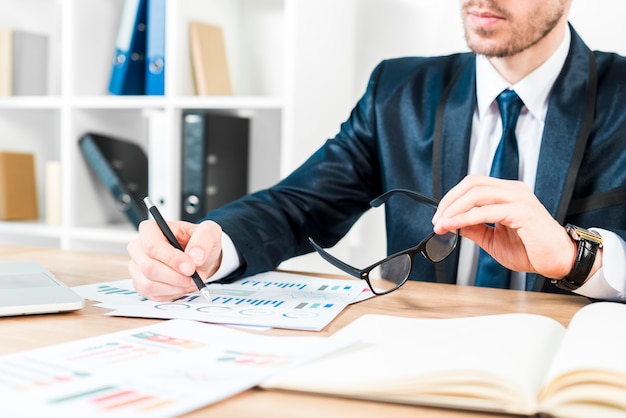 Photo close-up of a businessman analyzing the graph holding eyeglasses in hand