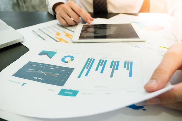 Close up of Businessman analyzing investment charts and using tablet on the desk.