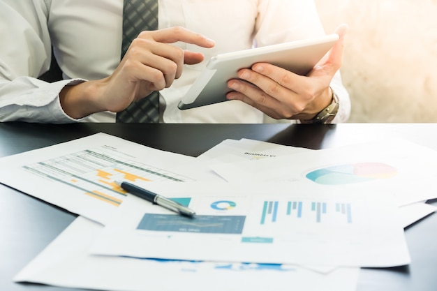 Close up of Businessman analyzing investment charts and using tablet on the desk.