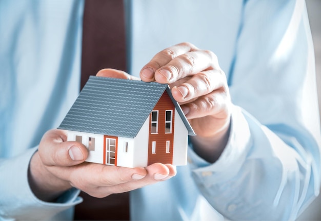 close up businessman in business suit holding a cute miniature house model using his both hands
