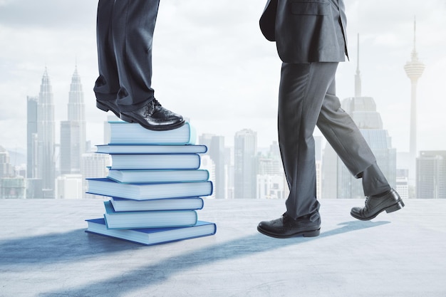 Close up of businessman and businesswoman feets and legs standing on top of stacked books Blurry city backdrop Education wisdom success growth and teamwork concept