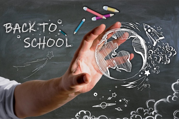 Крупный план руки бизнесмена, держащего абстрактный рисунок обратно в школу с карандашами и ракетой на фоне стены доски Концепция образования и знаний