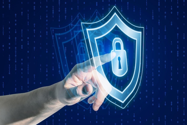 Close up of businessman hand pointing at creative digital security padlock and shield hologram on blurry blue binary code background Secure safety and identification concept