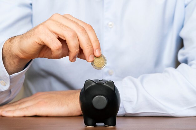 Close up of businessman hand putting coin into piggy bank. Saving money concept