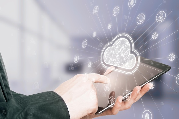 Close up of businessman hand using cellphone with digital white cloud hologram with various icons on blurry office interior background Cloud computing and storage server concept