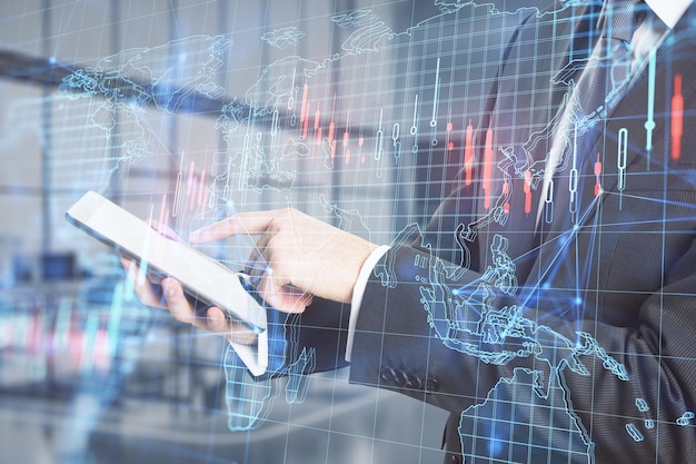 Close up of businessman hand using tablet with creative forex grid map on blurry office interior background Trade finance market and invest concept Double exposure