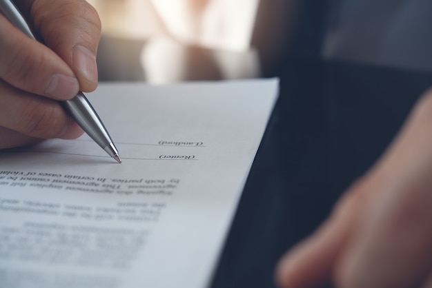 Foto chiuda in su della mano dell'uomo d'affari con una penna che firma il contratto di affari sul tavolo dell'ufficio