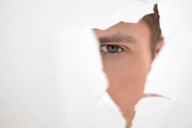 Close up businessman looking through a hole in the paper wallphoto with copy space