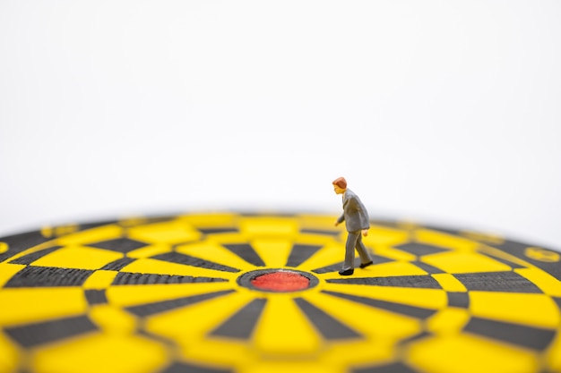 Close up of businessman miniature figure walking to center of  dart board with white.