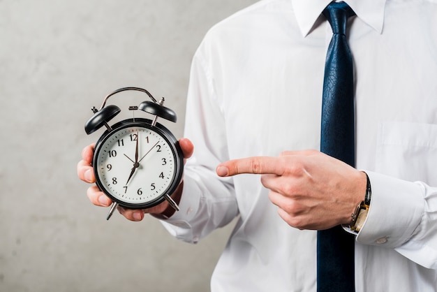 Close-up of a businessman pointing the finger at time against grey wall