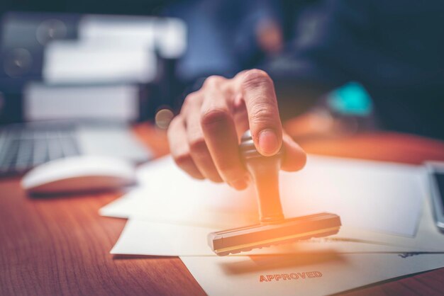 Photo close-up of businessman putting approved stamp on document in office