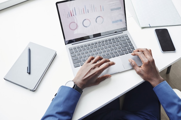 Photo close-up of businessman sitting at the table working with graphs on laptop online