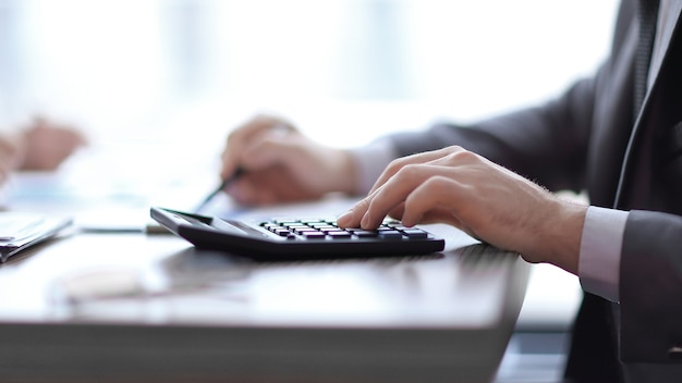 close up. the businessman uses the calculator sitting behind a Desk.